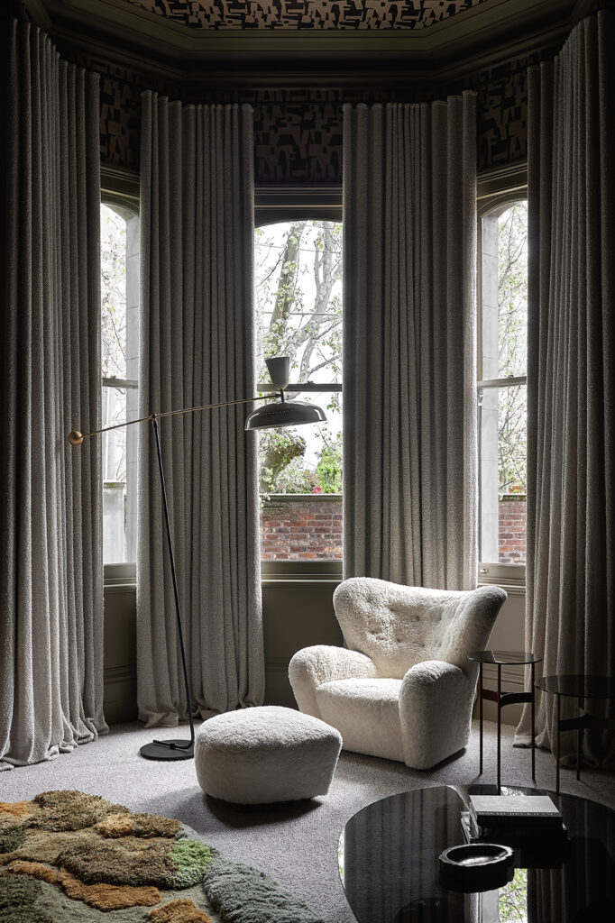 Simone Haag The Whiskey Room living room with cream curtains and with a cream armchair and cream pouf and green rugs