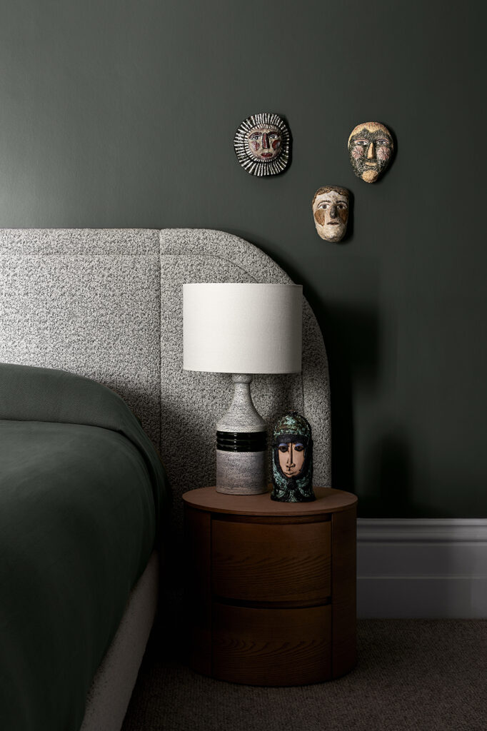 Simone Haag The Whiskey Room bedroom with green walls and with a bed with green grey headboard and with green bedding and with a wood round side table