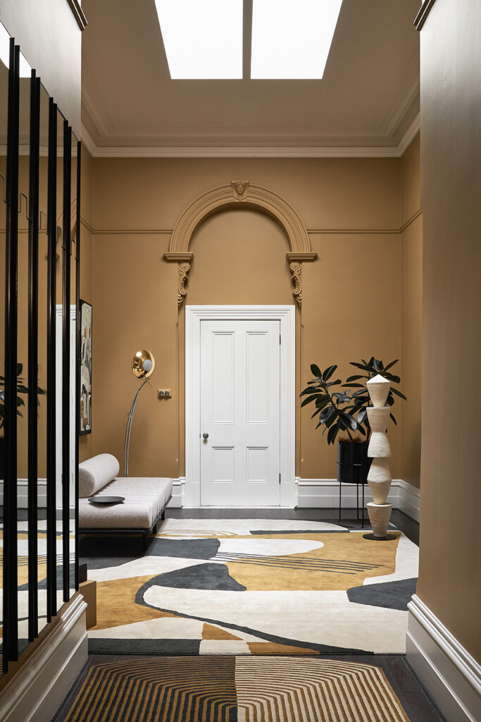 Simone Haag The Whiskey Room hall with mustard walls and with a white door that has a arch and a with a mustard and cream and black rug