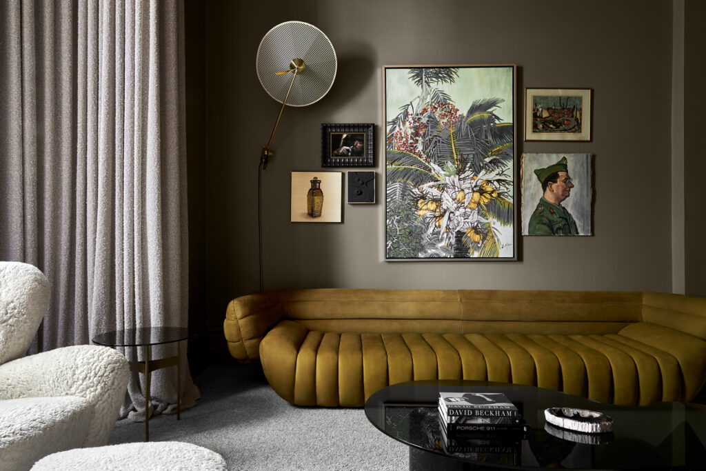 Simone Haag The Whiskey Room living room with a mustard couch and green walls with art hanging on the walls