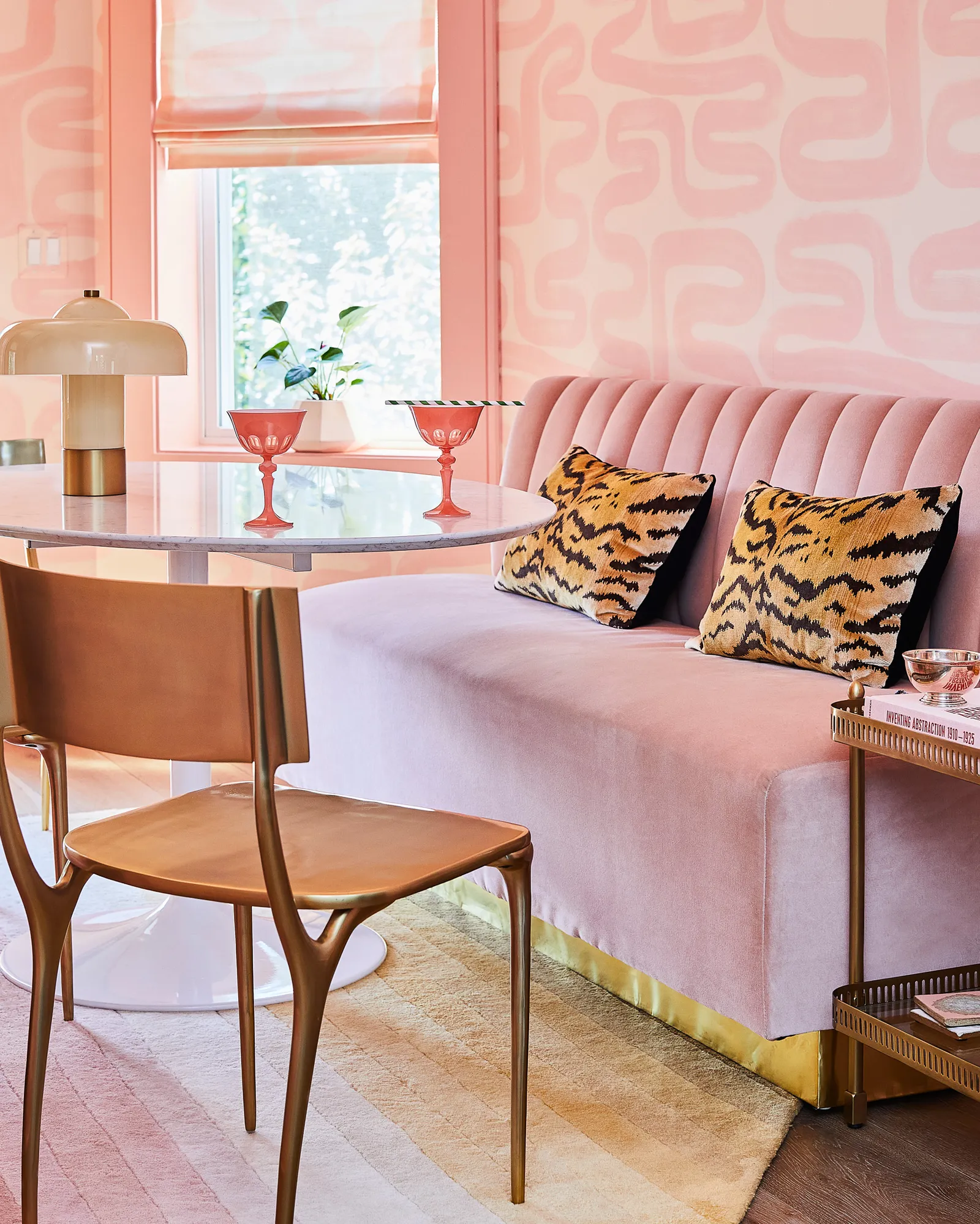 maximalist interior design dining room with a pink  abstract wallpaper and with a pink velvet bench and with a glass table