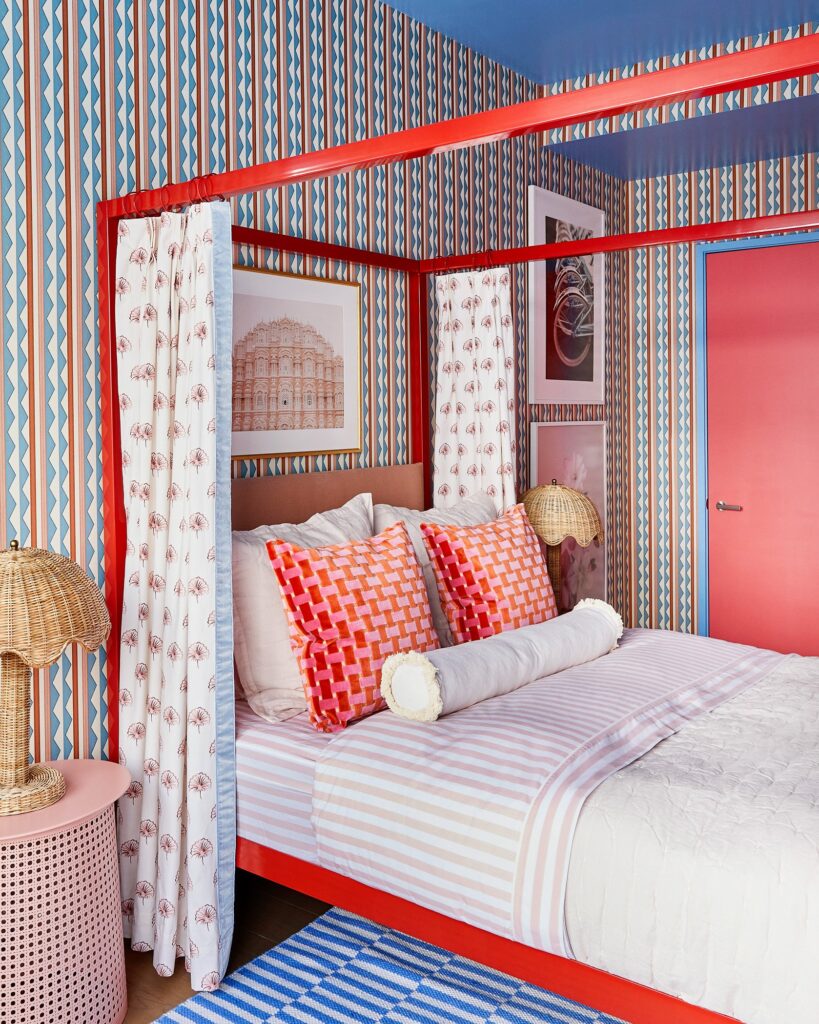 maximalist interior design bedroom with a geometric wallpaper and with a red dossel bed and with red pillows and with a pink bedside table