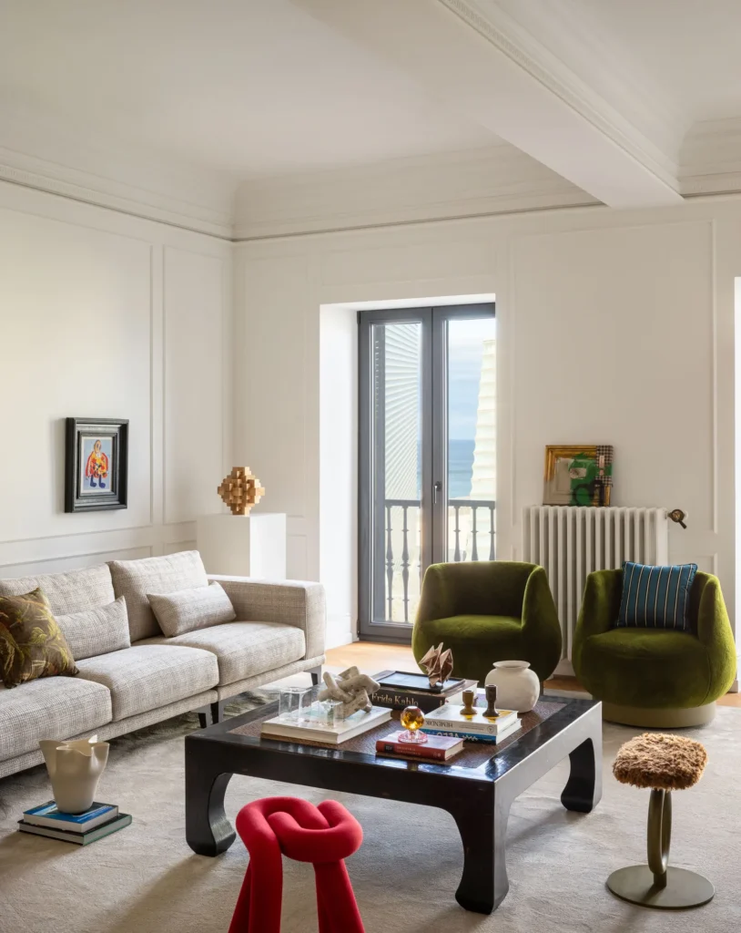 Contemporary Interior Design living room with a gray modern sofa and with velvet green armchairs and with a black wood center table and with decorative molding on the wall