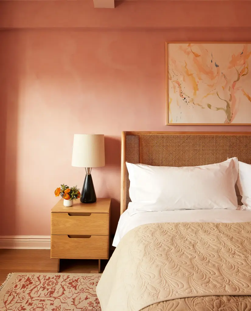 luxury apartment bedroom with pink walls and with a large rattan bed and with a wood bedside table and with a small lamp on the bedside table and with a textured rug