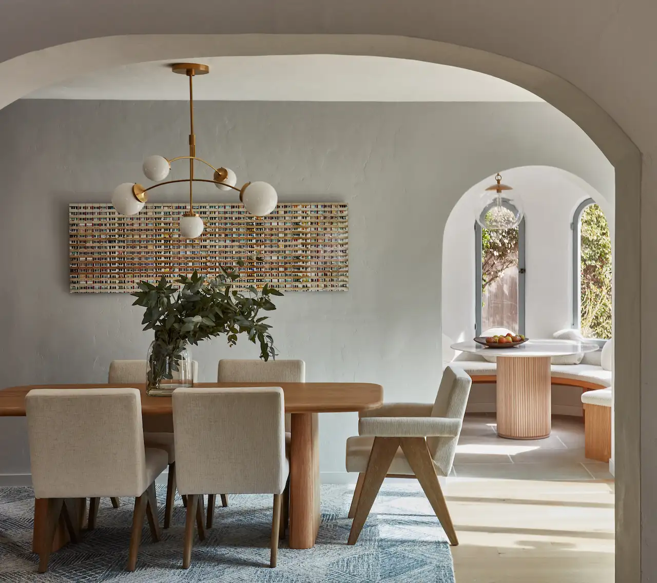 Earthy Interiors inspired dining room with cream walls and with an arched entry and with a large wood dining table and with linen and wood dining chairs and with a blue rug