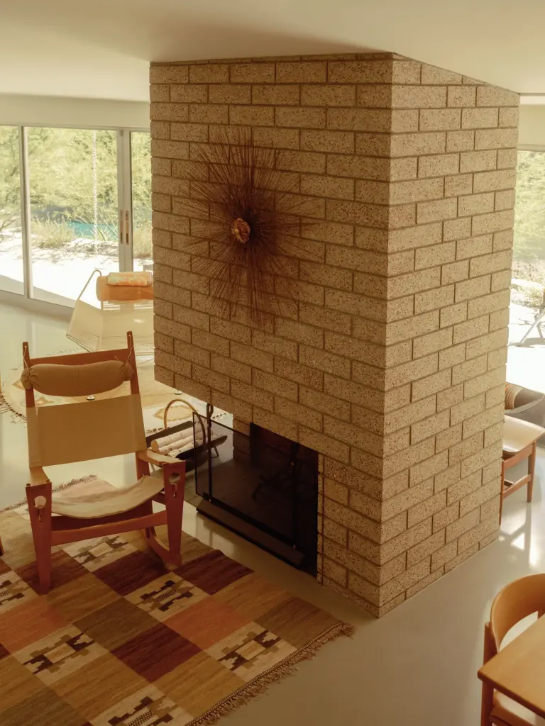 Mid-Century Modern house with large windows and with concrete floors and with a large brick fireplace and with a wooden chair and with a geometric rug