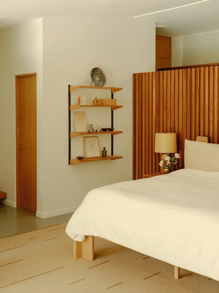 Mid-Century Modern house bedroom with clean cream walls and with concrete floors and with an wooden wall and with a large bed and with a wooden shelf and with a textured rug