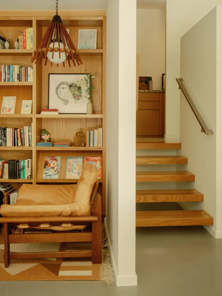 Mid-Century Modern house living room with clean cream walls and with concrete floors and with a wooden staircase and with a built-in wooden bookcase 