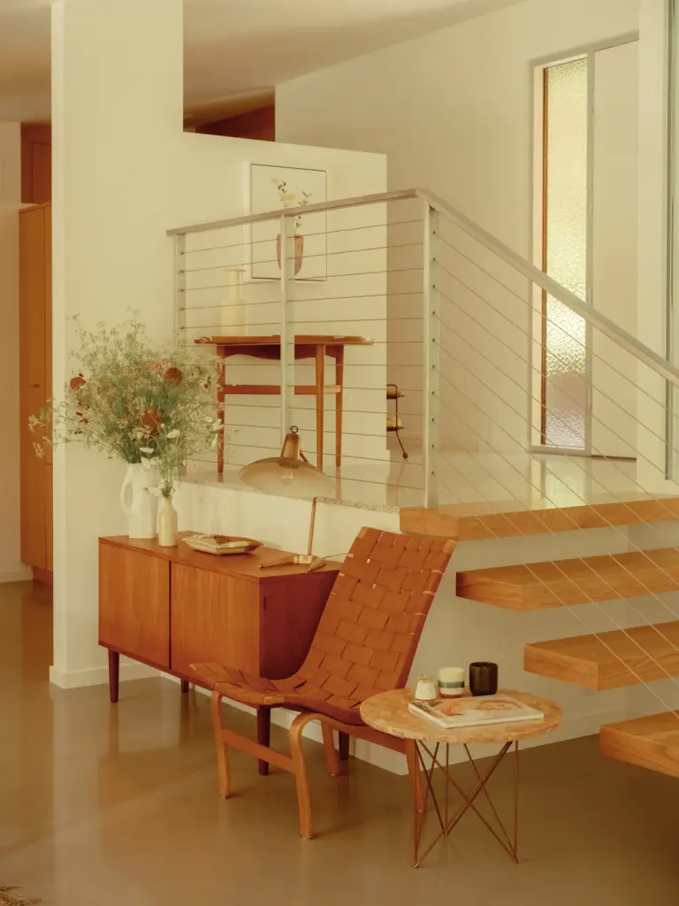 Mid-Century Modern house entryway with clean cream walls and with concrete floors and with wooden staircases and with a wood sideboard and with a leather chair