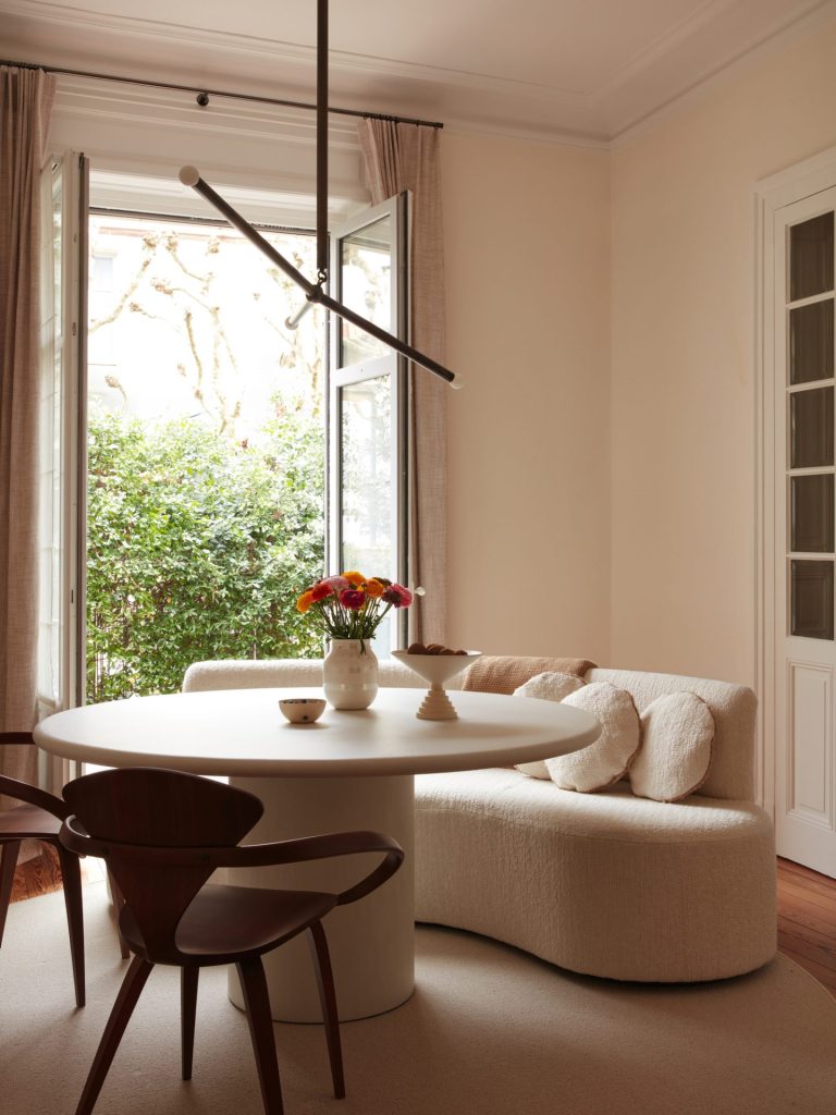 french villa dining room with cream walls and with a round travertine table and with wooden chairs and with a large bouclé sofa