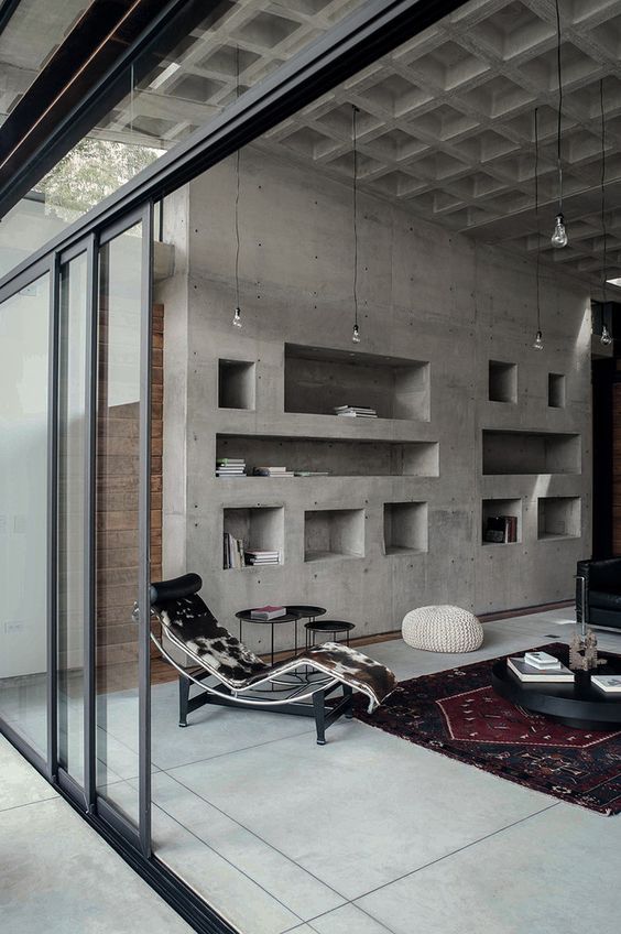 Raw Aesthetics in a living room with concrete walls and with concrete floors and with large windows and with a leather armchair and with a large textured rugs