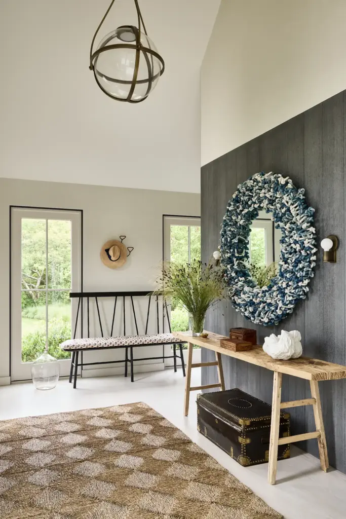 Organic Modernism style entryway with a large window and with a wooden wall and with a wood console table and with a rounded mirror and with a wood and fabric bench and with a textured rug