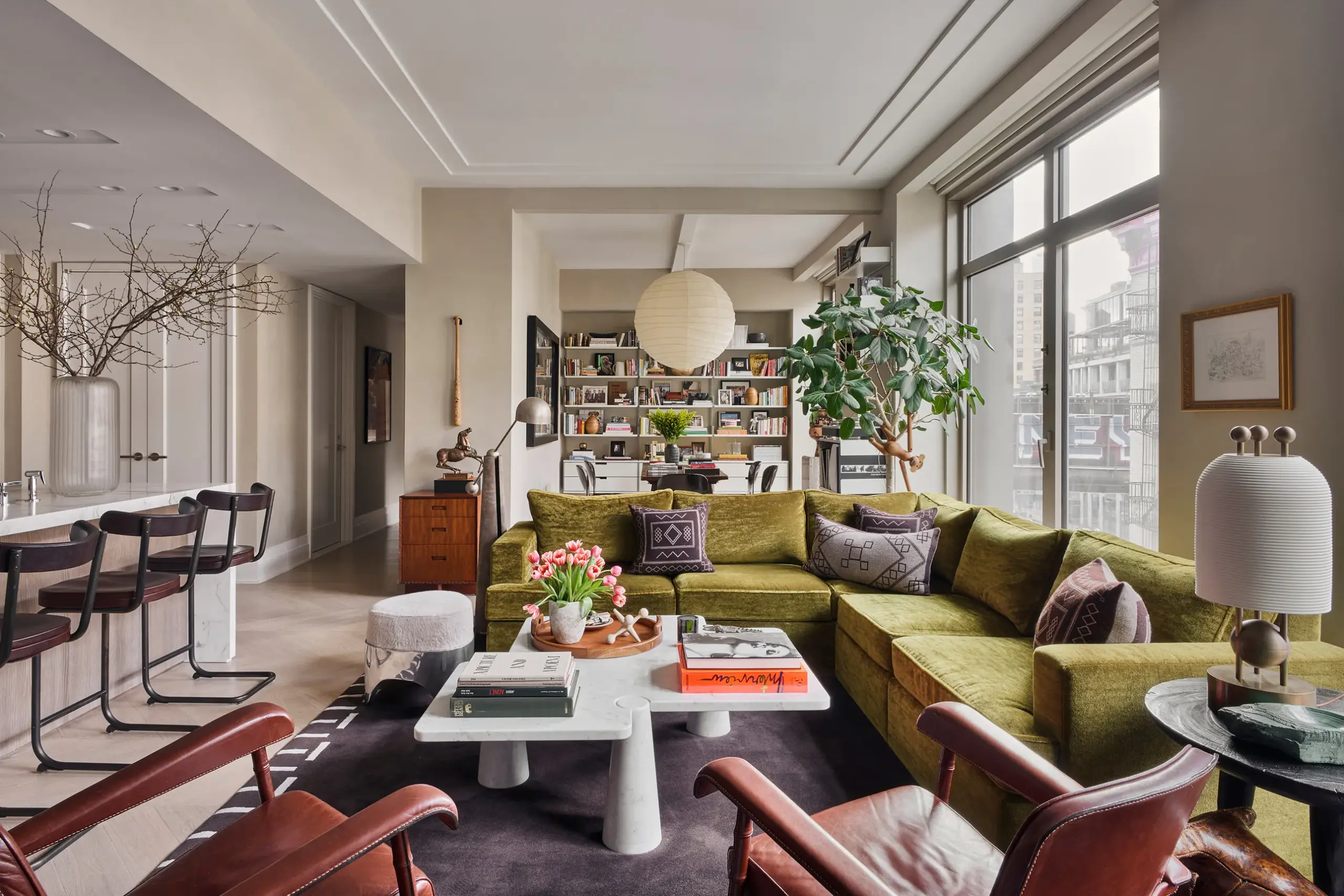 Antoni Porowski living room with cream walls and with large windows and with a wood sideboard and with an indoor tree and with a marble center table and with a velvet green sectional sofa and with a dark rug