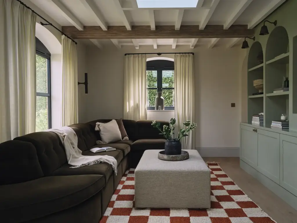 Organic Modernism style living room with cream walls and with large windows and with a large brown velvet sofa and with a grey fabric center table and with a chequered rug