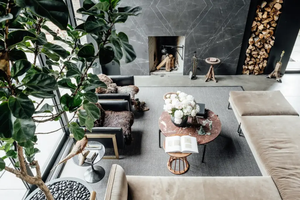 Raw Aesthetics in a living room with a concrete floor and with a black marble fireplace and with a large cream sectional sofa and with leather armchairs and with a marble center table