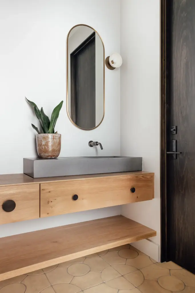 Raw Aesthetics in a bathroom with white walls and tiled floors and with a wood and concrete lavatory and with an oval mirror