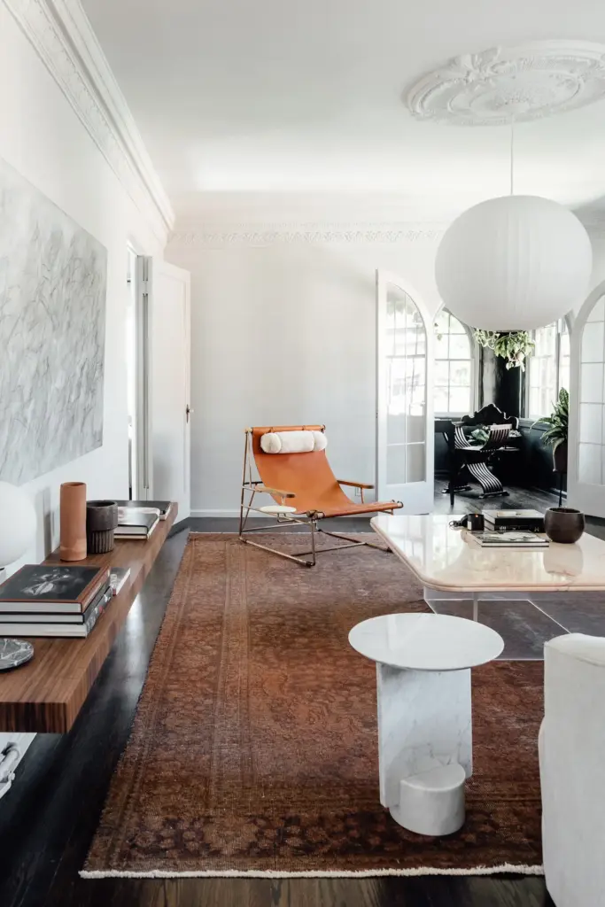 Raw Aesthetics in a living room with concrete floors and with white walls and with a leather armchair and with a stone side board and with a wood shelve