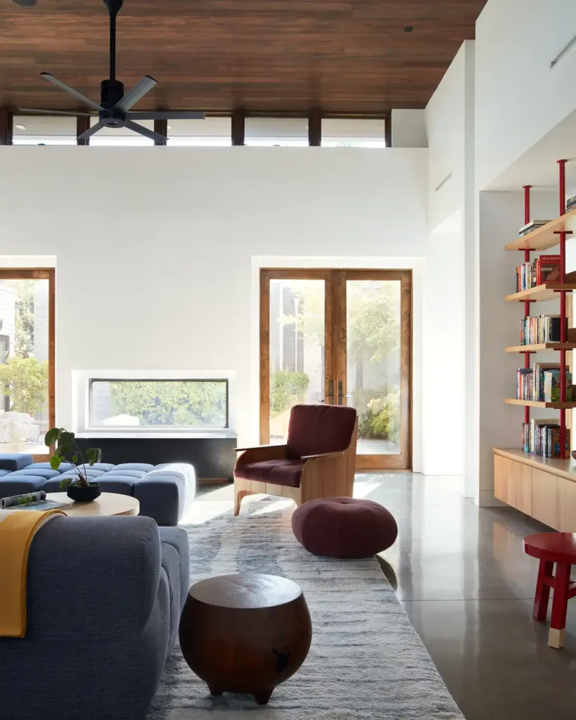 Organic Modernism style living room with cream walls and with a wood ceiling and with large windows and with a wood bookcase and with a large sofa and with a brown armchair and with wood side tables