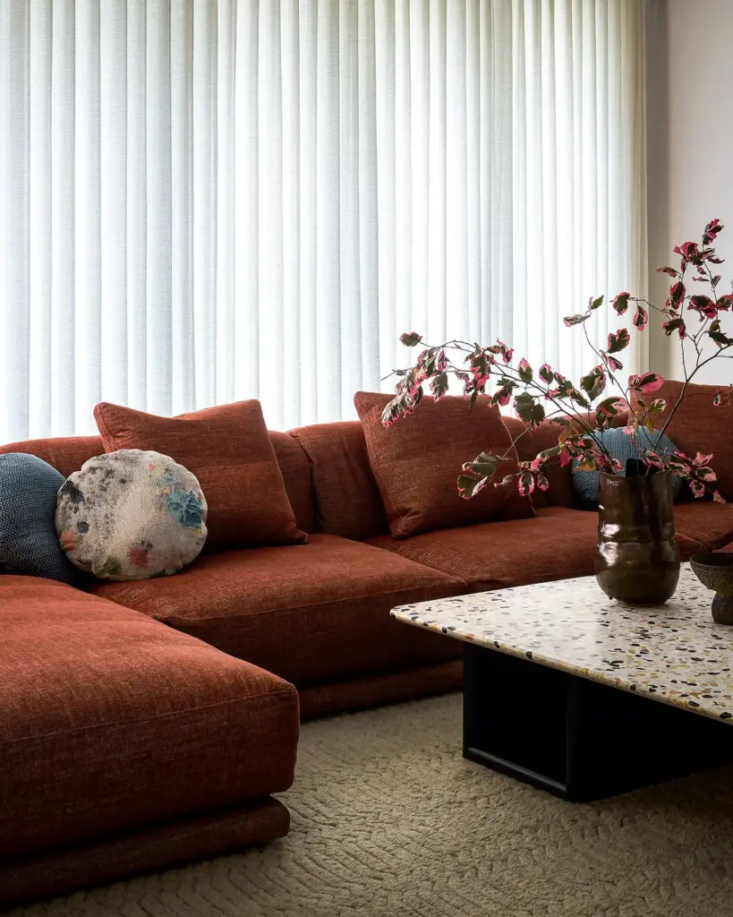 Organic Modernism style living room with large windows and with cream walls and with a large terracotta sectional sofa with textured pillows and with a stone and wood center table