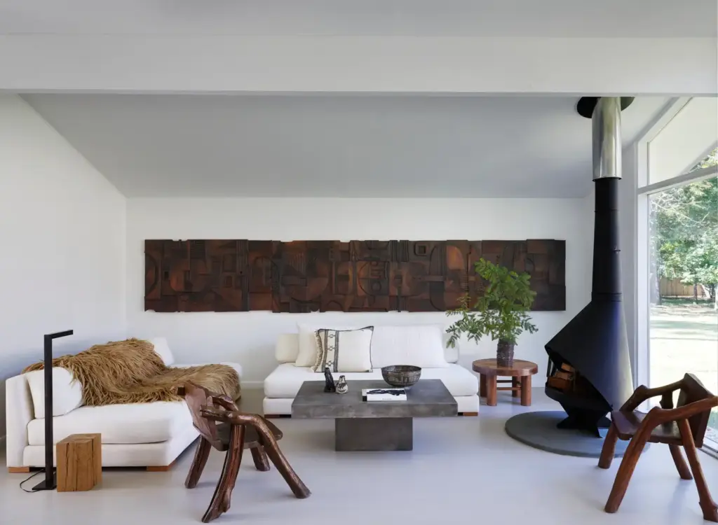 Raw Aesthetics in a living room with concrete floors and with a black iron fireplace and with a concrete center table and with a large sectional sofa and with wood armchairs