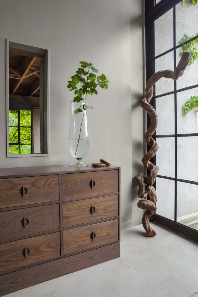 Raw Aesthetics in a entryway with concrete walls and floors and with a large window with black frames and with a large wood sideboard