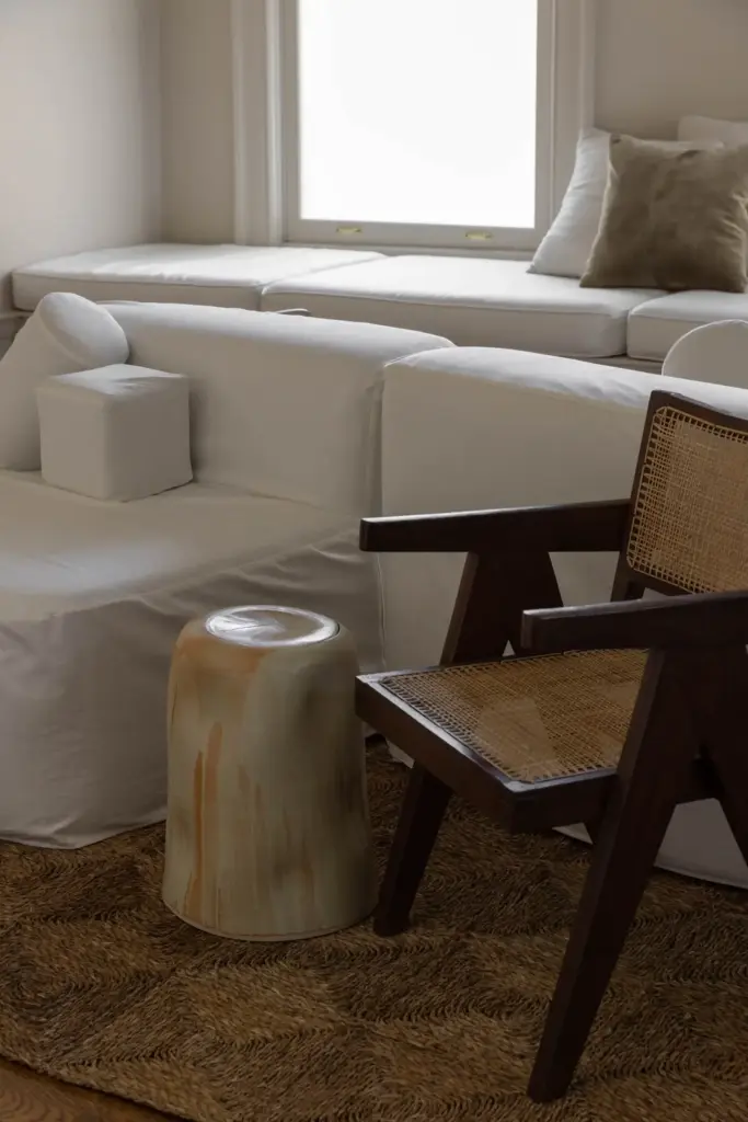 Raw Aesthetics in a living room with cream walls and with a large linen sofa and with a ratan armchair and with a wood side table and with a jute rug