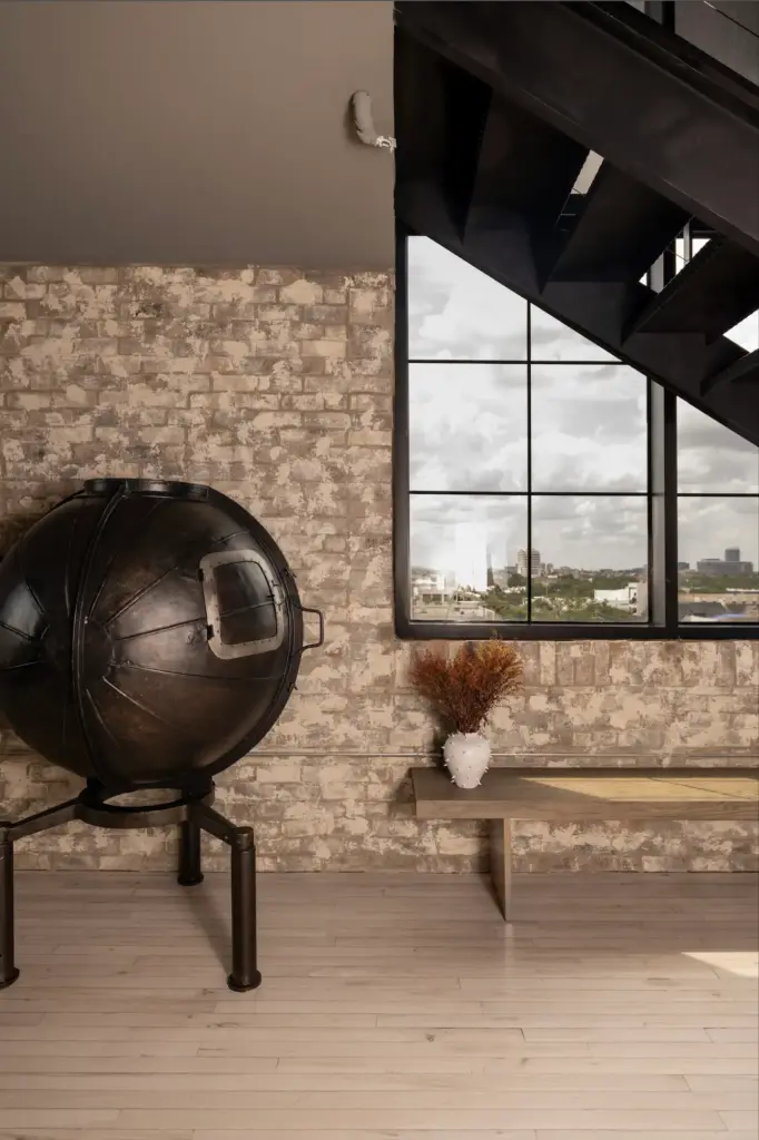 Raw Aesthetics in a living space with wooden floors and with brick walls and with black iron staircases and with a wood bench and with a large iron sculpture