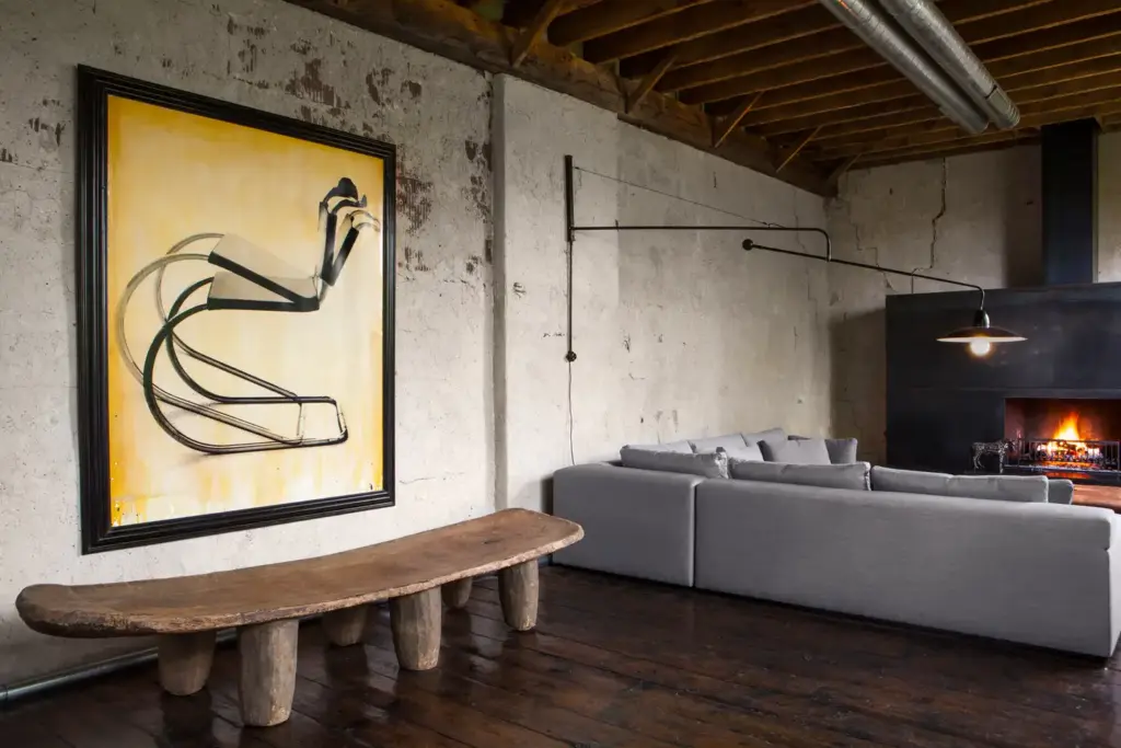 Raw Aesthetics in a living room with wood floors and ceiling and with a concrete walls and with a large wood bench and with a grey sectional sofa and with a black iron fireplace