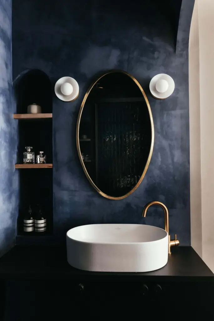 small apartment decor ensuite with dark blue walls and with black cabinets and with a golden round mirror