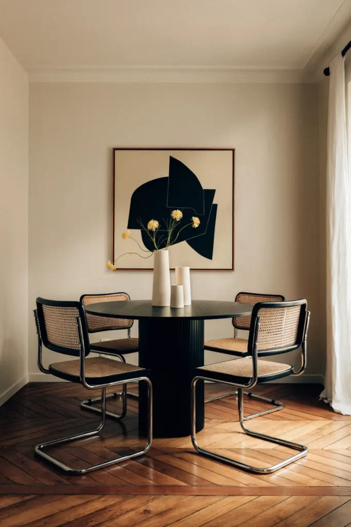 small apartment decor dining area with cream walls and with wood floors and with a black round dining table and with mid-century modern dining chairs and with a painting framed on the wall