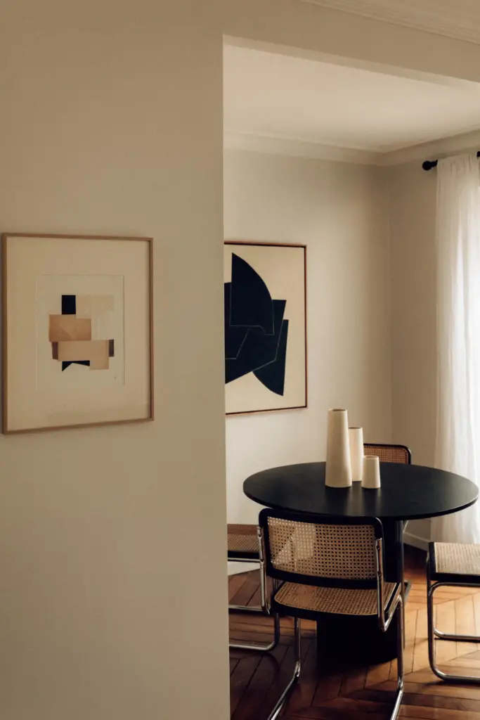 small apartment decor dining area with cream walls and with wood floors and with a black round dining table and with mid-century modern dining chairs and with a painting framed on the wall