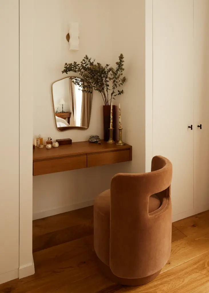 French interior design home bedroom corner with cream walls and with a wood desk and with a golden mirror and with a velvet armchair