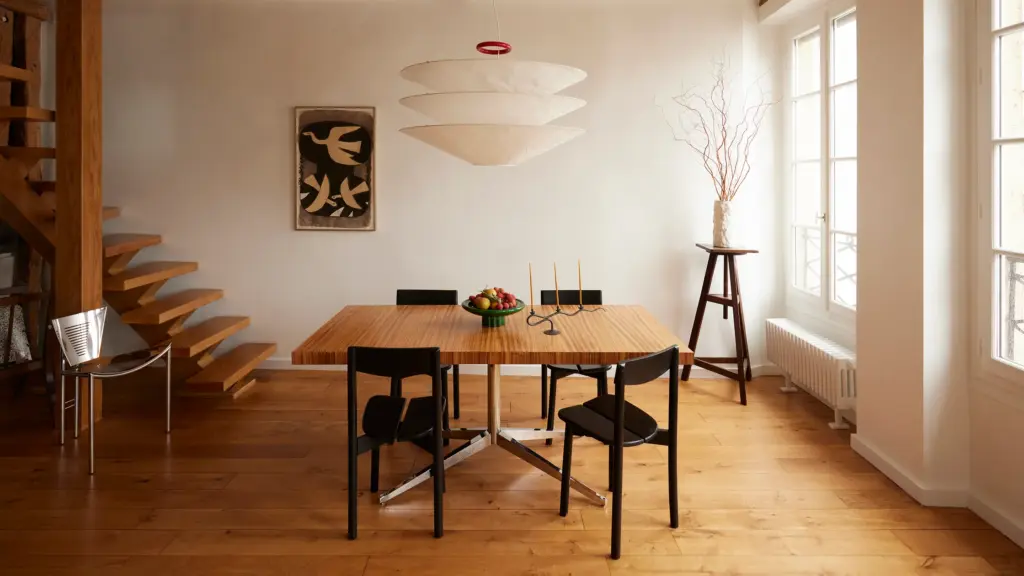 French interior design home dining room with cream walls and with a wood dining table and with black dining chairs and with a cream ceiling lamp