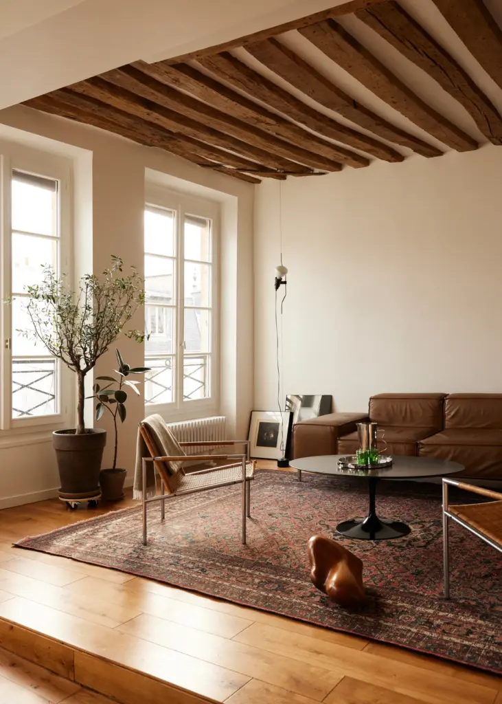 French interior design home living room with cream walls and with wood exposed beams and with a leather sofa and with a brown rug and with a round center table