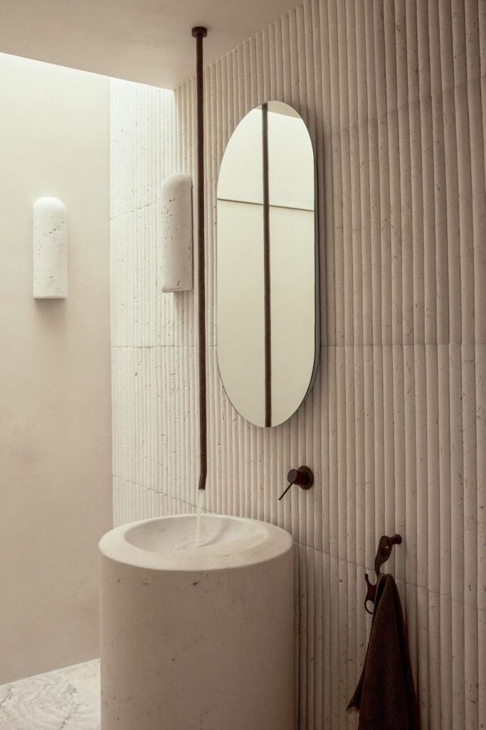 minimalist architecture bathroom with cement walls and with a textured feature on the main wall and with an oval mirror