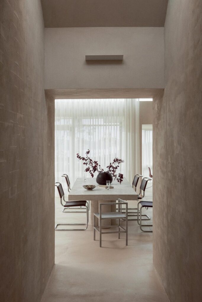 minimalist architecture dining room with cement walls and with a large window and with a large travertine dining table and with dining chairs