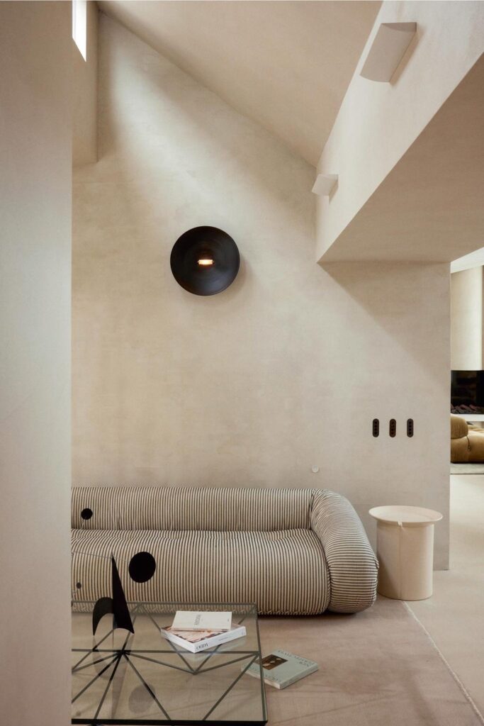 minimalist architecture living room with cream cement walls and with an inclined ceiling and with a large curved sofa and with a glass center table