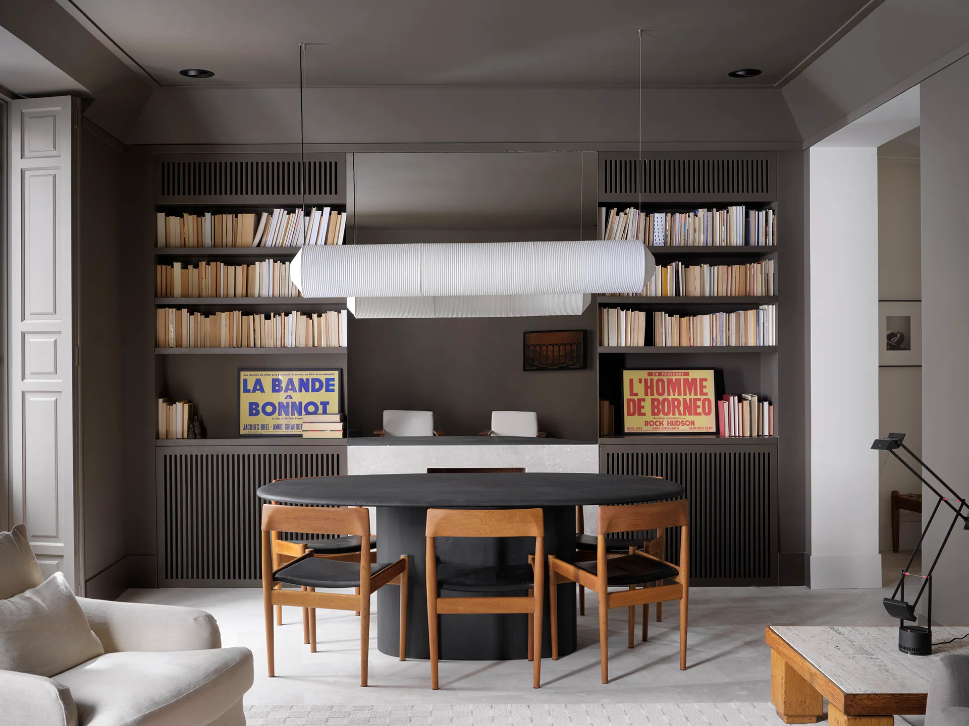 minimalist interior design living and dining room with grey walls and with a custom bookshelf and with a black dining table and with wood dining chairs