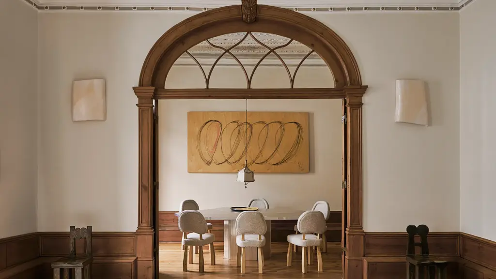 eclectic interior design dining room with cream walls and with an wooden arched entry and with a marble dining table and with classic dining chairs and with a canvas painting hanging on the main wall