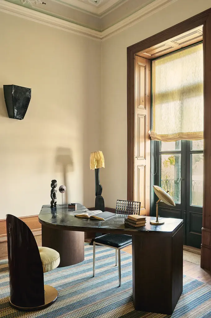 eclectic interior design home office with cream walls and with a large window and with a crved wood desk and with a blue rug