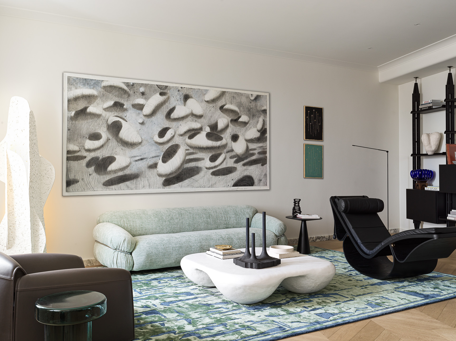 This image showcases minimalist home decor with a focus on clean lines and neutral tones. A plush mint green sofa anchors the space, while a unique cloud-like coffee table and modern art add sculptural elements. The black accent chair and shelving provide contrast, completing the sophisticated, minimalist design.