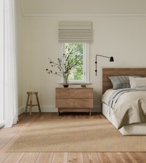 Neutral bedroom with light wood furniture & a woven area rug. Sheer curtains soften the bright window, adding a serene touch.