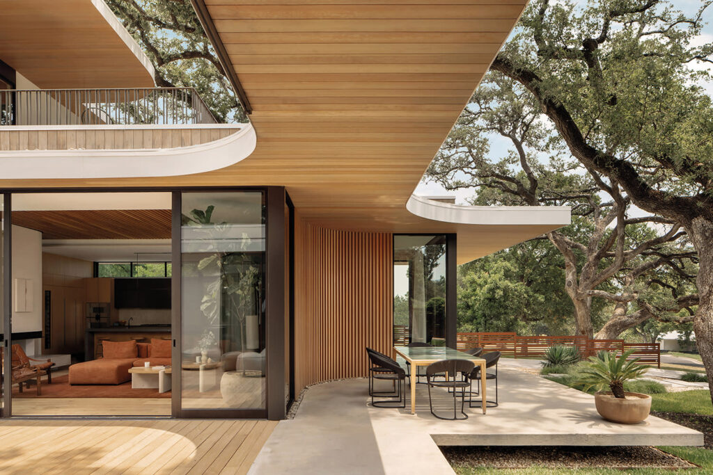 A natural home with a terrace overlooking a lush garden. The home features a wooden ceiling, sliding glass doors, and a dining area.