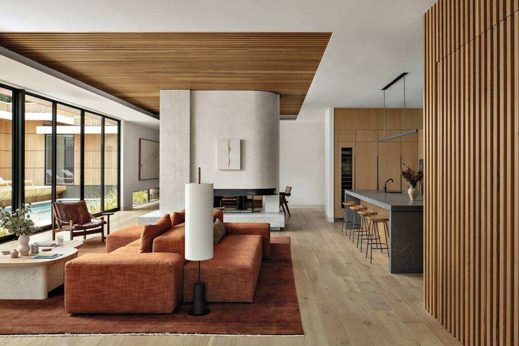 A spacious natural home living area with a fireplace, comfortable seating, and a view of the outdoors. The area features a mix of textures and natural elements.