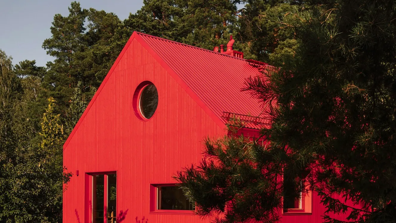 A striking red house with a circular window stands out among the green trees. Its vibrant color and unique design create a captivating contrast.