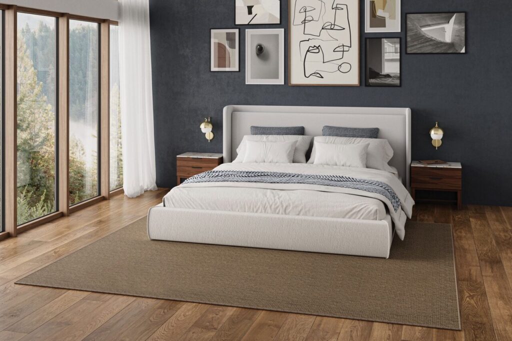 A neutral area rug grounds a modern bedroom with a gallery wall, dark accent wall, and large windows with a nature view. Serene and stylish.