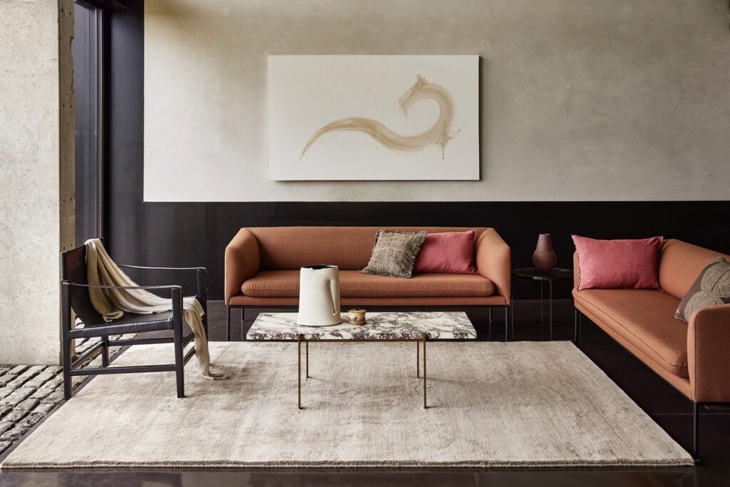 A textured area rug anchors a modern living room with warm-toned sofas, a marble coffee table, and abstract art. Stylish and inviting space.